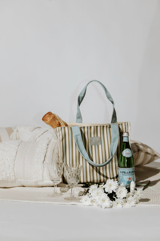 Striped tote bag with a bottle of wine, glasses, and flowers on a white surface.