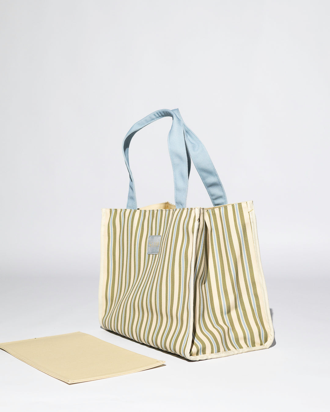 Side view of striped blue, green and beige tote bag with a light blue handles. Willow versa bag