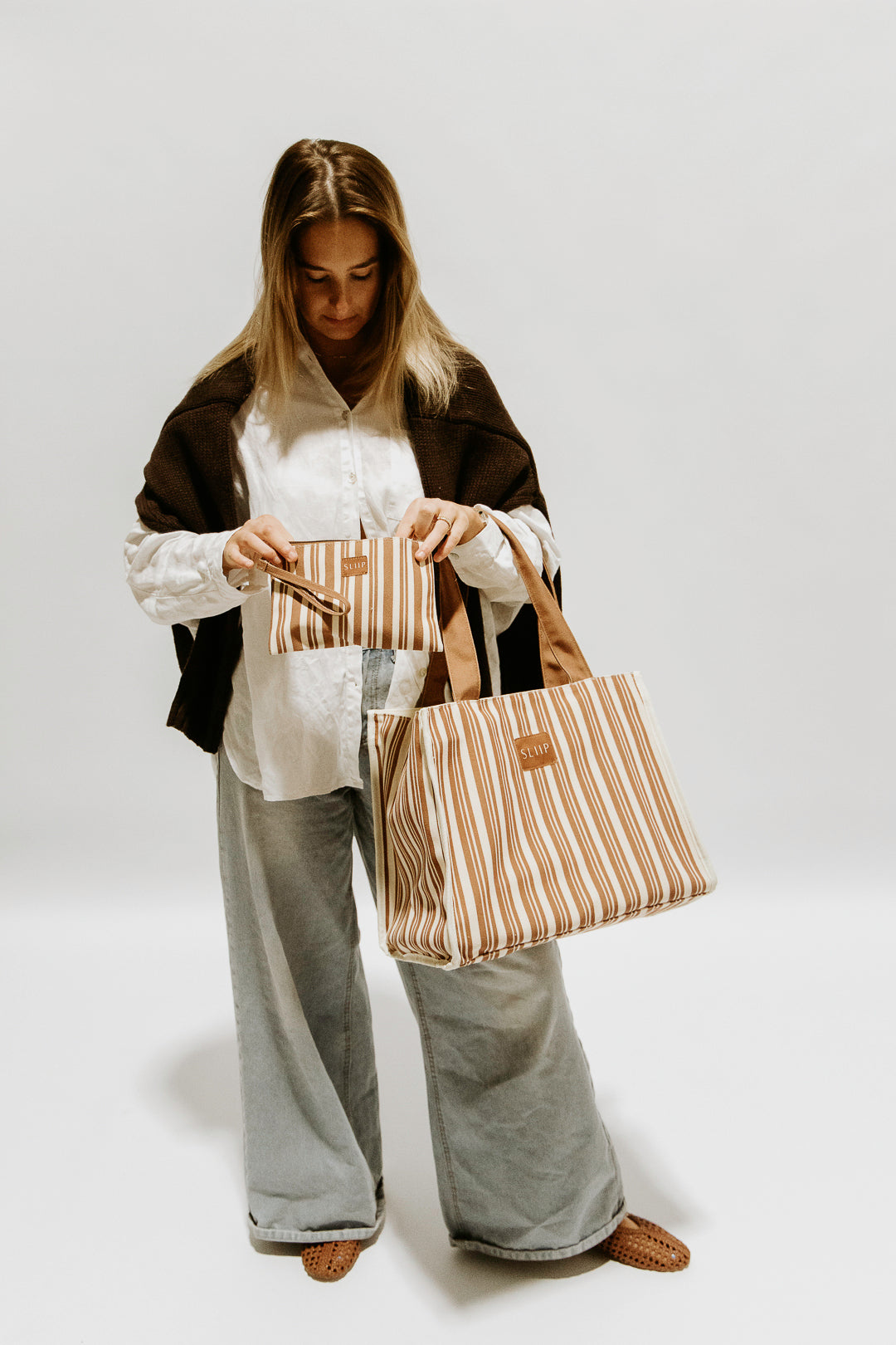 Woman holding two brown and beige striped bags, small and large bag