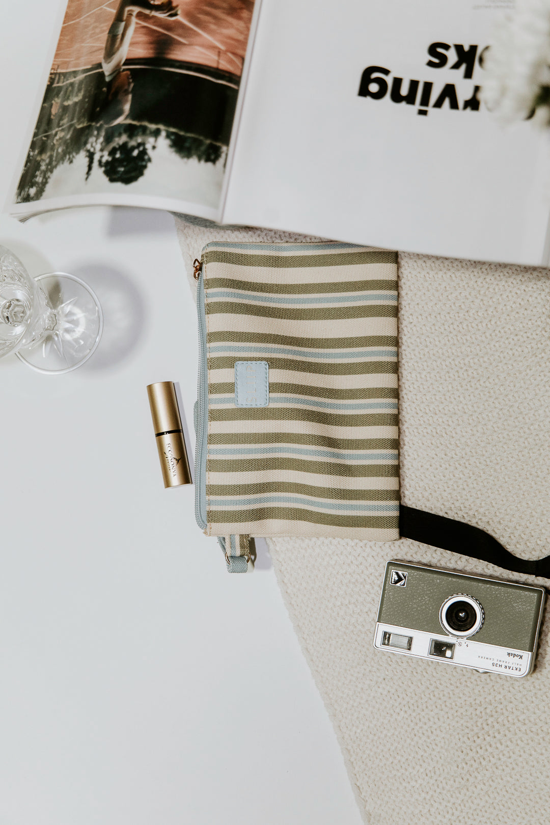 top view of blue, green and beige small pouch bag with blue handle and light blue zip next to magazine