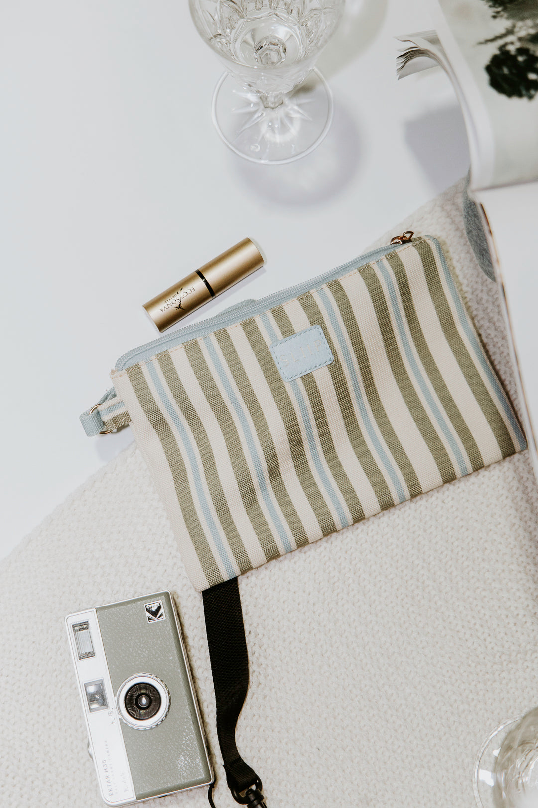 blue, green and beige small pouch bag with blue handle and light blue zip, with camera and  lipstick inside