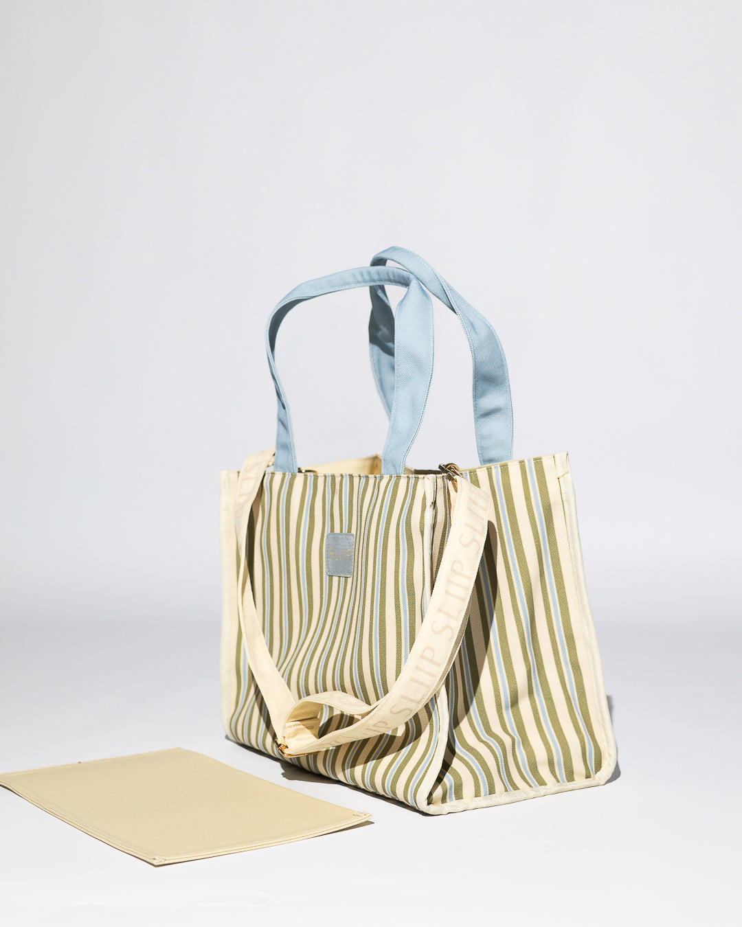 Striped blue, green and beige tote bag with a light blue handles and a SLIIP branded shoulder strap. Unstructured with base out 