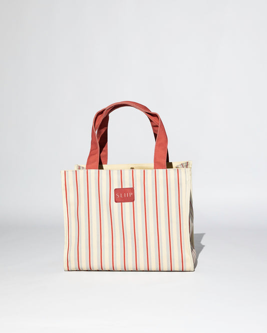 Striped red, blue and beige tote bag with red handles on a light gray background