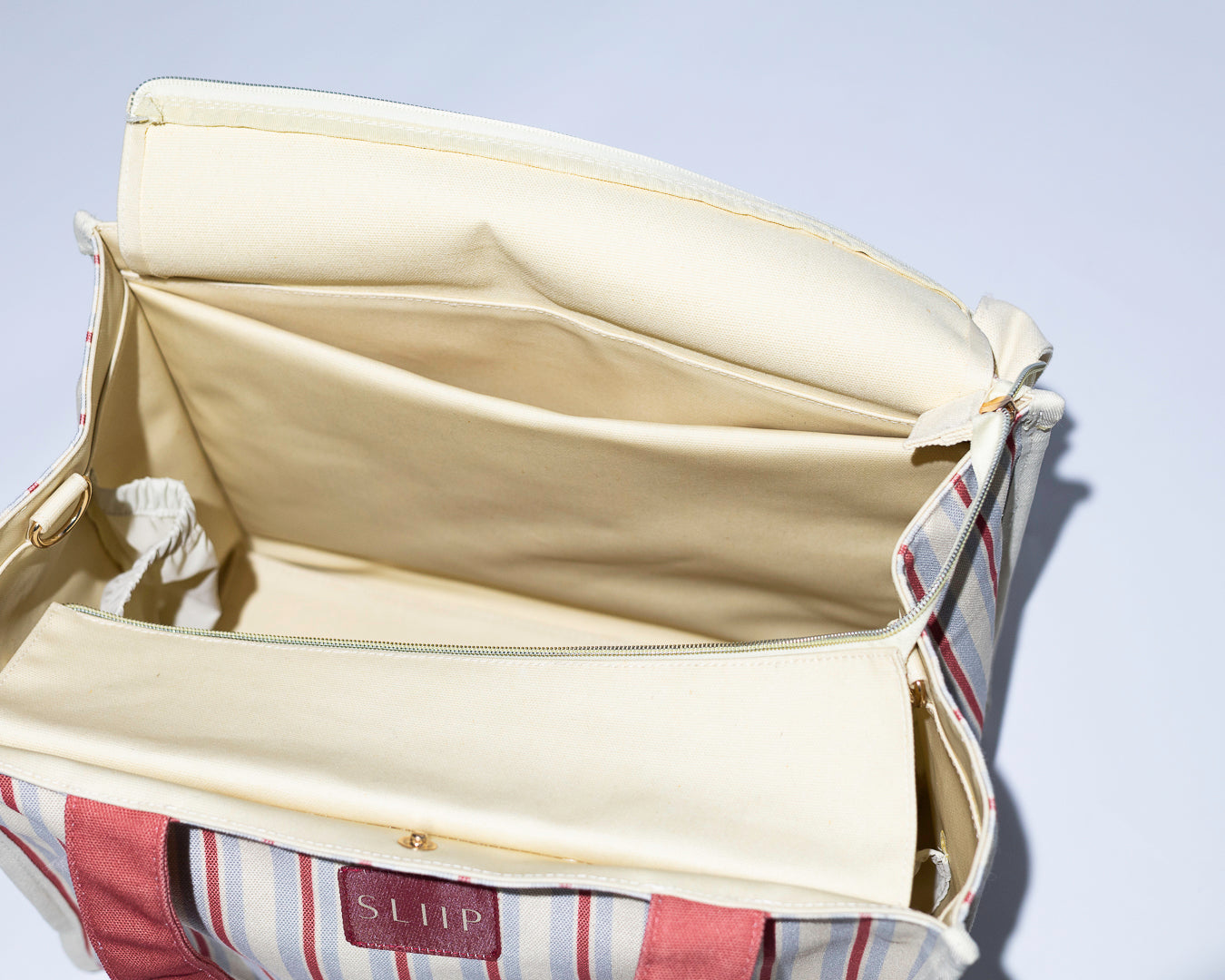 Inside view of tote bag, open beige bag with striped lining, showing inside compartments