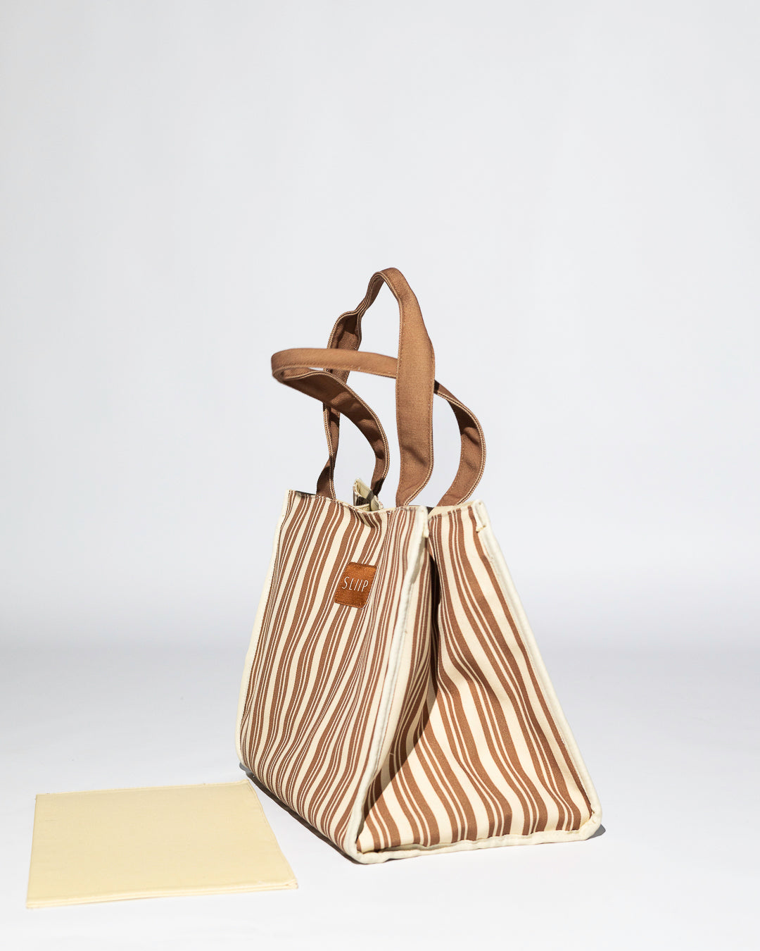 side view of brown and beige striped tote bag with brown handles, showing unstructured mode wth base out